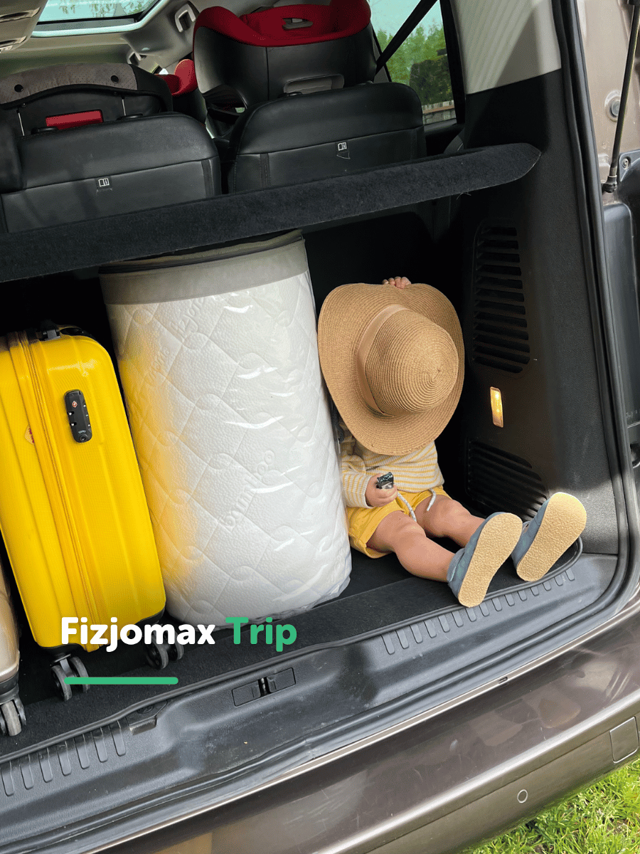 Dziecko siedzące w bagażniku obok spakowanego materaca Fizjomax Trip